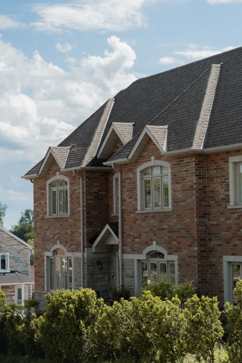 Charming brick house with gable roof surrounded by lush greenery under a clear blue sky.